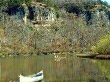A canoe on still water with rocky cliffs and bare trees in the background.